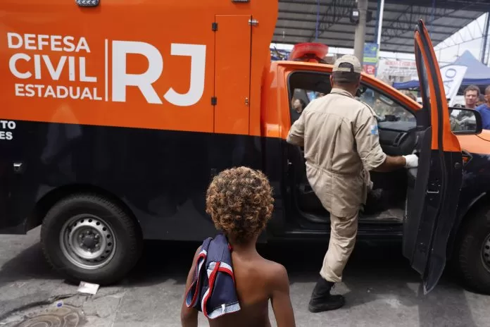 Rio de Janeiro (RJ), 29/10/2025 - Uma criança observa um funcionário da prefeitura entrar no carro dio IML, durante protesto de moradores contra execuçoes na comunidade da Vila da PenhaOperação Contenção.